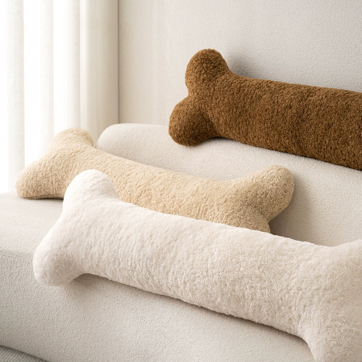 Bone-shaped bouclé pillows in three colors on a sofa